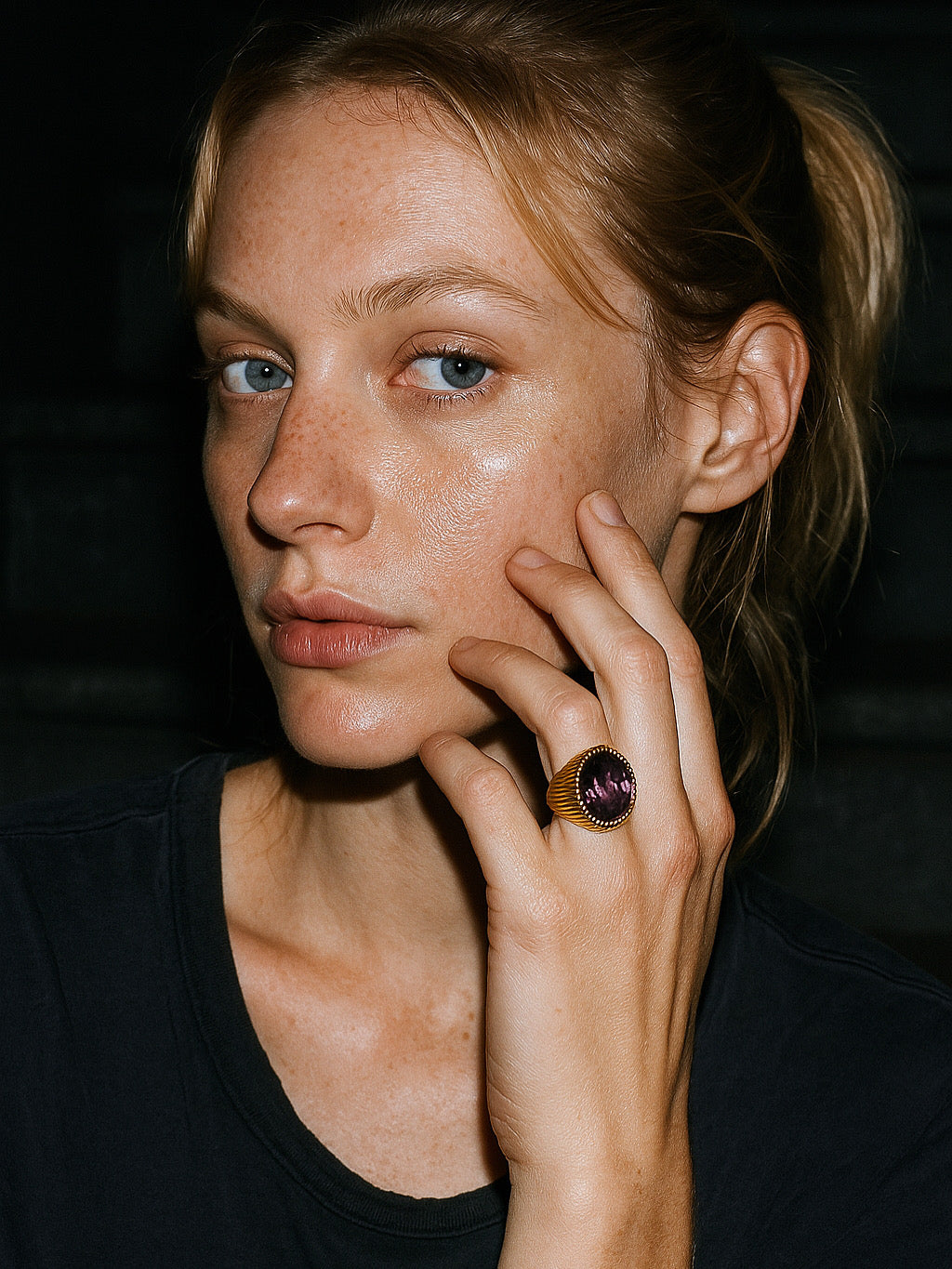 Woman wearing a ring with a purple gemstone against a dark background